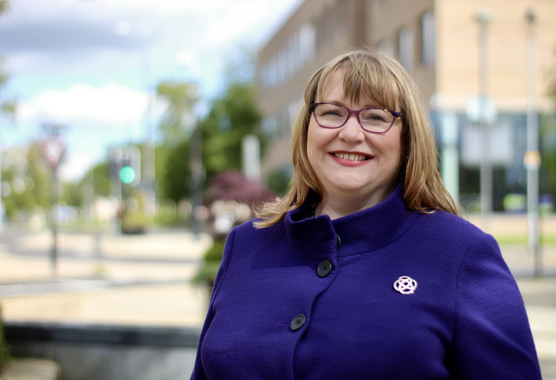 Clare Adamson MSP wearing a purple coat stands in front of the Houldsworth Centre on Kenilworth Avenue in Wishaw.