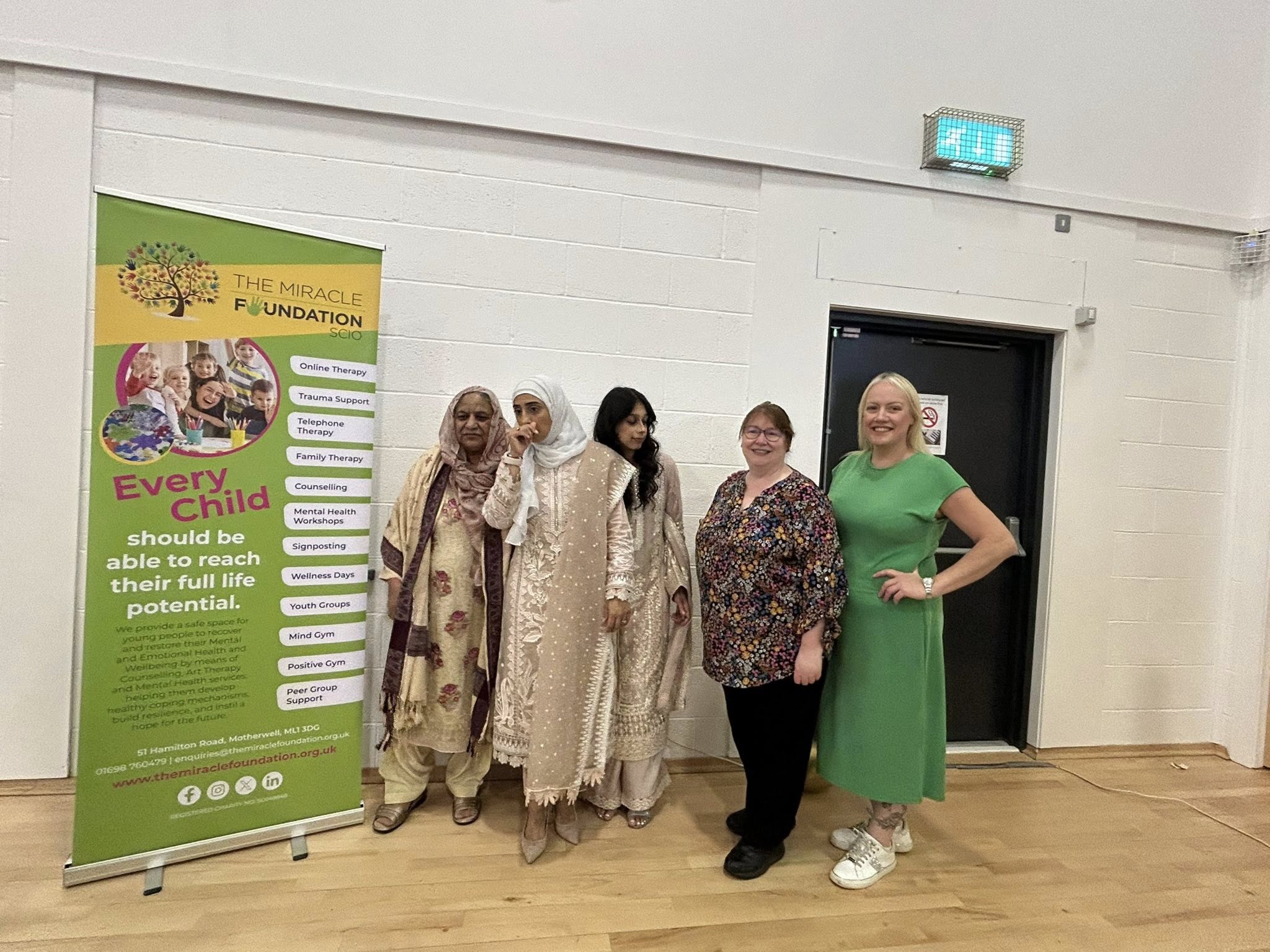 Clare Adamson MSP stands with attendees beside a banner for The Miracle Foundation at the Forgewood Community Centre during an Eid celebration.